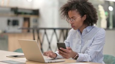 Ofiste akıllı telefon ve dizüstü bilgisayar kullanan çalışkan Afrikalı iş kadını 