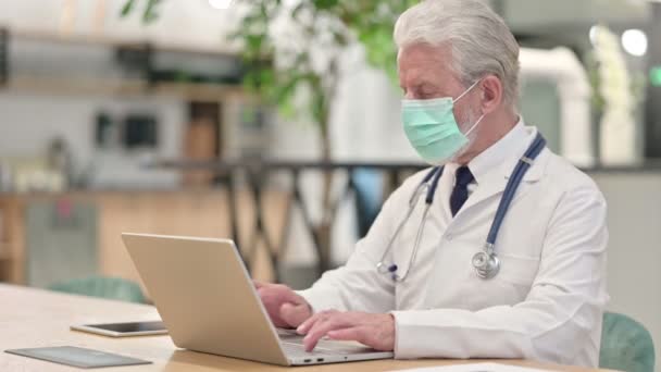 Starší starý lékař s obličejovou maskou pracuje na notebooku — Stock video