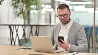 Ofiste akıllı telefon ve dizüstü bilgisayar kullanan sıradan bir genç. 