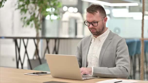 Hombre joven casual con el ordenador portátil sonriendo en la cámara en la oficina — Vídeos de Stock