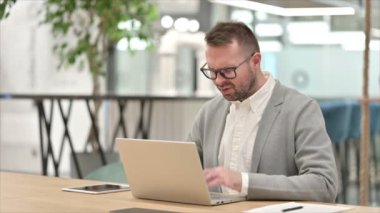 Dizüstü bilgisayarı olan stresli genç adamın başı ağrıyor.