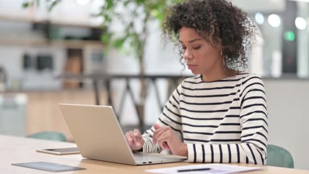 Mujer de negocios africana con portátil que tiene dolor de cuello en la oficina — Vídeos de Stock