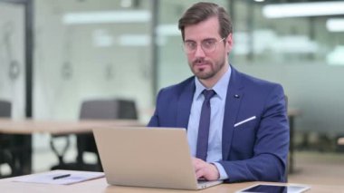 Dizüstü bilgisayarlı Ciddi Genç İş Adamı Kameraya Bakıyor