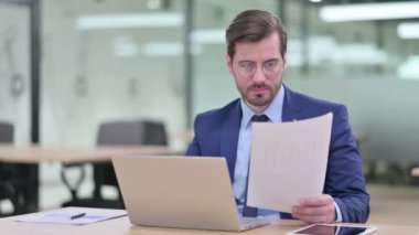 Belgelerle birlikte dizüstü bilgisayarda çalışan Ciddi İşadamı 