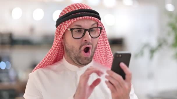 Izgatott fiatal arab férfi ünnepli siker Smartphone — Stock videók