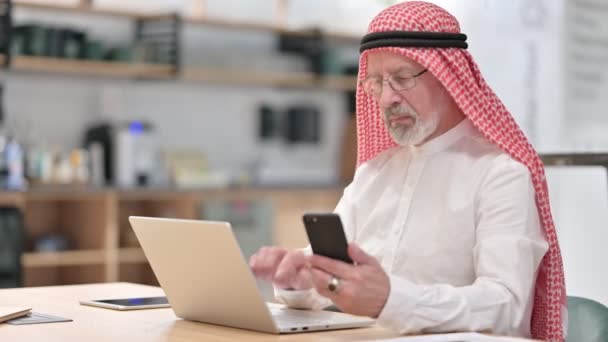 Старый арабский бизнесмен работает над ноутбуком и смартфоном — стоковое видео