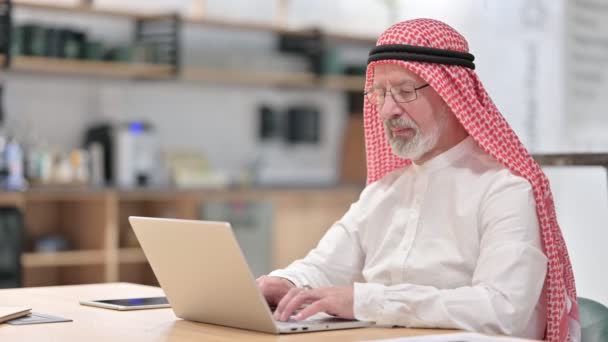 Старый арабский бизнесмен с ноутбуком улыбается в камеру — стоковое видео