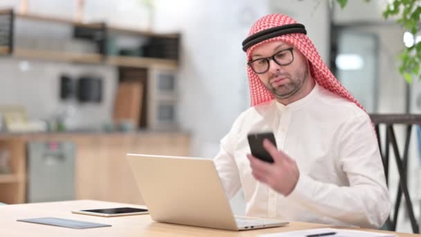 Молодой араб с ноутбуком разговаривает на смартфоне в офисе — стоковое видео