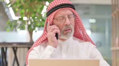 Dizüstü bilgisayarlı yaşlı Arap İşadamı Smartphone ile konuşuyor 