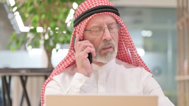 Oude Arabische zakenman met laptop aan het praten op smartphone — Stockvideo