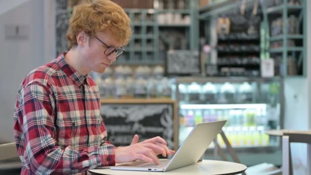 Mladý rusovlasý muž s notebookem v kavárně s bolestí zápěstí 