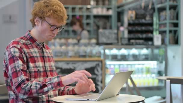 咖啡店使用笔记本电脑的红头发年轻人背痛 — 图库视频影像