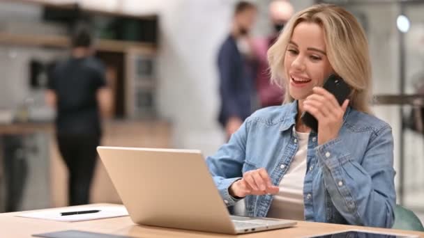Junge Gelegenheitsfrau mit Laptop spricht bei der Arbeit mit Smartphone — Stockvideo