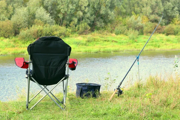 Fishing chair, rod and bait on the river bank in autumn