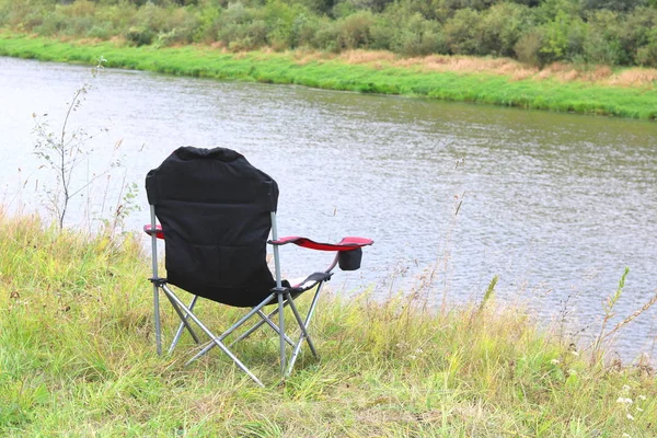 便携式折叠旅游红色扶手椅在绿草在河附近的野餐夏季 — 图库照片