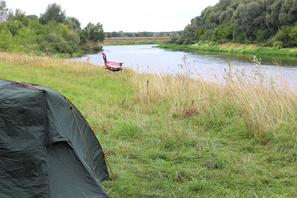 便携式折叠旅游红色扶手椅和旅游帐篷在绿草在绿色的夏天在河边野餐 — 图库照片