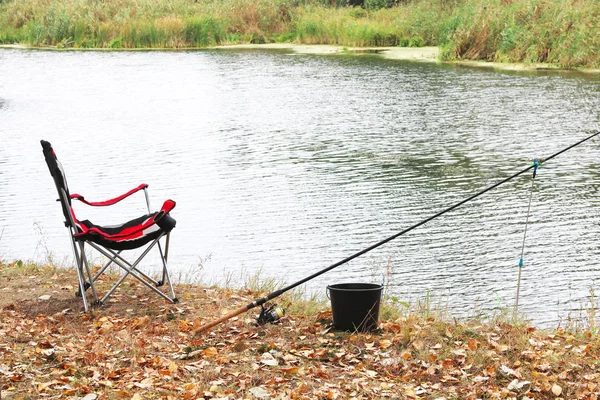 川岸に1本の棒と快適な折りたたみ観光椅子を持つスポーツ夏の釣り — ストック写真