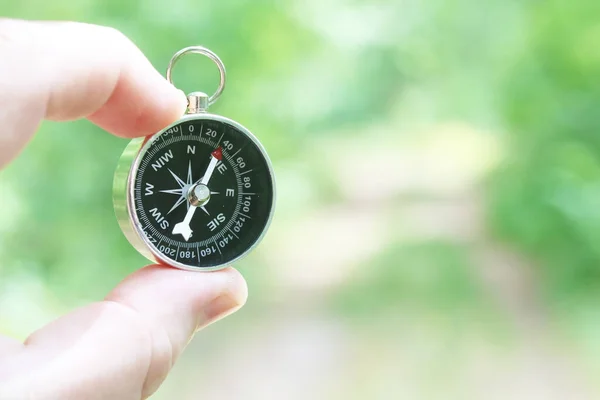 Old classic navigation compass in hand on natural background as symbol of tourism with compass, travel with compass and outdoor activities with compass