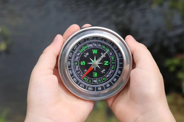 Old classic navigation compass in hands on natural background as symbol of tourism with compass, travel with compass and outdoor activities with compass