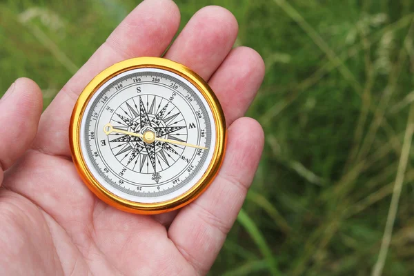 Old classic navigation compass in hand on natural background as symbol of tourism with compass, travel with compass and outdoor activities with compass