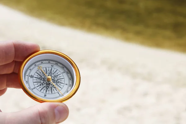 classic navigation compass in hand in summer against background of sandy beach as symbol of tourism with compass, travel with compass and outdoor activities with compass