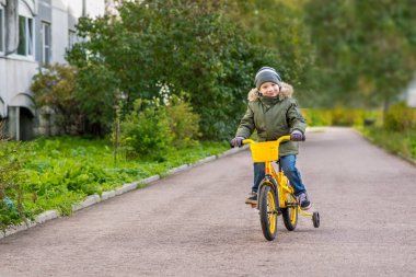 neşeli çocuk yeşil ceketli sarı bisiklet sürmek