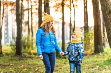 Anne ve oğlu sarı şapka ve mavi ceket parkta yürümek
