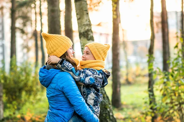 mom in a yellow hat and a blue jacket hugs her son in a yellow hat and a blue jacket autumn forest