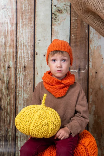 Un garçon dans une écharpe orange et un chapeau est assis avec une citrouille — Photo