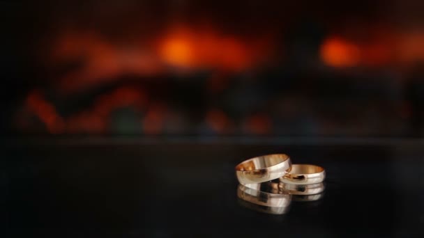 Статична рамка Два золоті кільця проти вогню з каміна Скляний стіл чорний темний фон — стокове відео