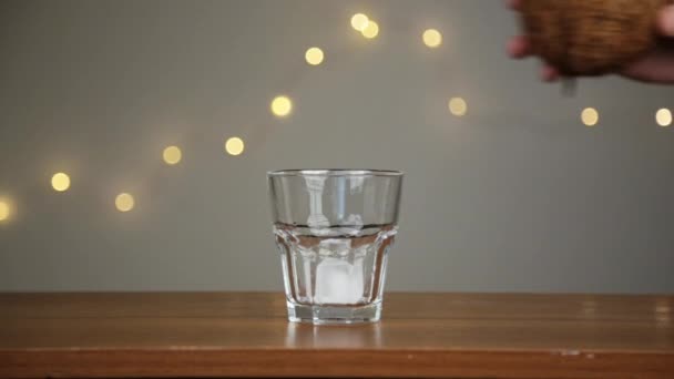 Człowiek rzuca lód w szklankę, a następnie wylewa wodę kokosową. Na tle świateł — Wideo stockowe