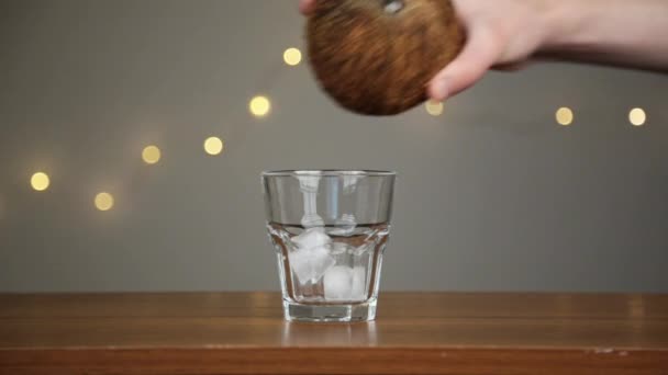 O homem atira gelo para um copo e depois derrama água de coco. Contra o fundo das luzes — Vídeo de Stock