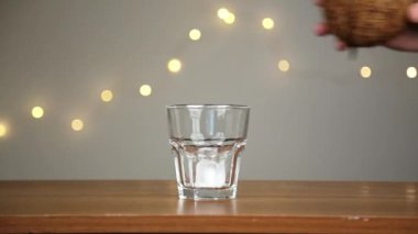 Adam bir bardağa buz atar, sonra hindistan cevizi suyu döker. Işıkların arka planına karşı