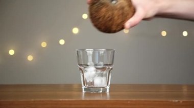 Adam bir bardağa buz atar, sonra hindistan cevizi suyu döker. Işıkların arka planına karşı