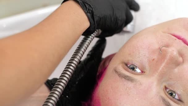 美容師はピンクの染料から女性の髪を洗浄します。流行中のホームサロン. — ストック動画