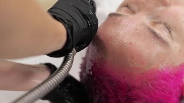 Η κομμώτρια πλένει τα μαλλιά μιας γυναίκας από μια ροζ βαφή. Σπίτι σαλόνι κατά τη διάρκεια της επιδημίας. — Αρχείο Βίντεο