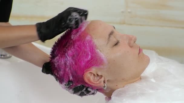Η κομμώτρια πλένει τα μαλλιά μιας γυναίκας από μια ροζ βαφή. Σπίτι σαλόνι κατά τη διάρκεια της επιδημίας. — Αρχείο Βίντεο