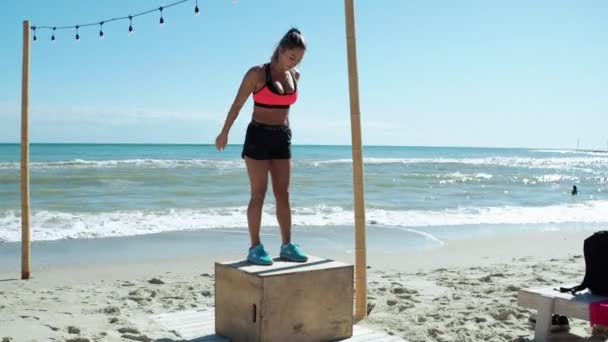 Blond kvinna tränar ben Hoppa på lådan Crossfit med en tränare På stranden — Stockvideo