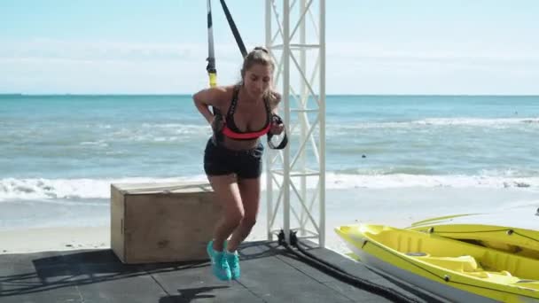 금발 여자가 해변에서 트레이너와 함께 크로스 피트로 달리는 다리를 훈련 시킨다 — 비디오
