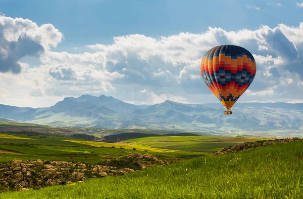Balão de ar quente colorido voando sobre o campo verde — Fotografia de Stock