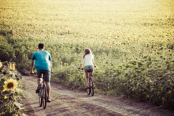 Teen couple riding bike in sunflower field — Stock Photo, Image