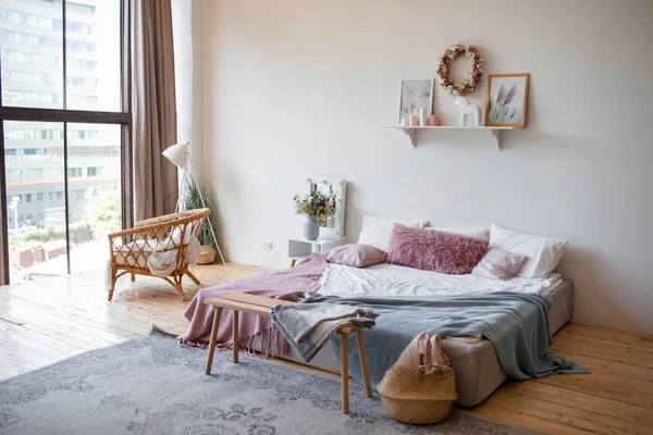 真正的照片明亮舒适的卧室内部与全景窗 木制地板上的王床 灰色的地毯 白色的墙壁与生态主题的海报 窗前的柳条椅 — 图库照片