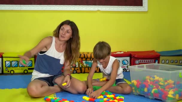 Kleine zoon met mam speelt constructeur op de tapijt puzzel in de speelkamer. — Stockvideo