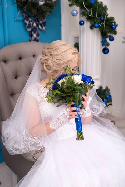 A young bride in a white dress is sniffing her wedding bouquet that is carefully held by her hands