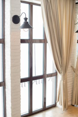 Pencerenin arka planında bir lamba ve perdeli bir duvar..