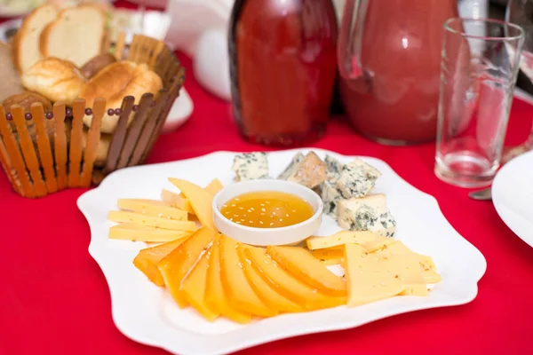 Honey and cheeses on a white plate, food. On the red table.