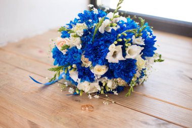 Mavi kasımpatı, frezya, güller ve şakayıklardan oluşan güzel bir modern düğün buketi. Tahta arka planda. Yüzüklerle yeni evliler.