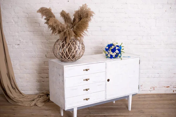 White wood bedside table, dresser in bedroom. bridal bouquet on the nightstand vase with flowers. interior. Series of furniture loft style. Modern designer. Vintage style short cabinet with drawer in the room.