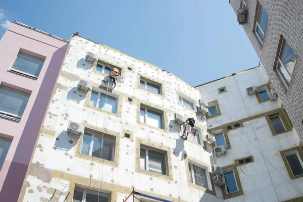 Dış duvar panelinin termal yalıtımı. İşçi, yüksek duvarlı bina yalıtıyor.