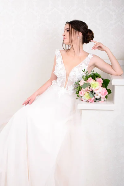 Стройная красивая женщина в роскошном свадебном платье на белом студийном фоне. Великолепная невеста с цветами. — стоковое фото
